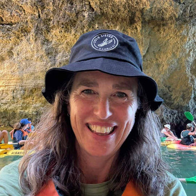 Person wearing a blue bucket hat with a logo, smiling in front of a rocky cave background.