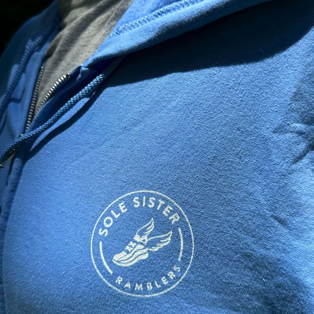 Close up Sole Sister Rambler logo on the chest of a light blue zip up hoodie.