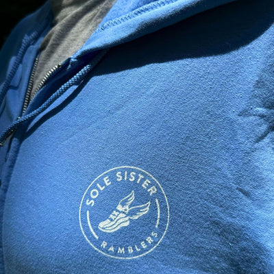 Close up Sole Sister Rambler logo on the chest of a light blue zip up hoodie.