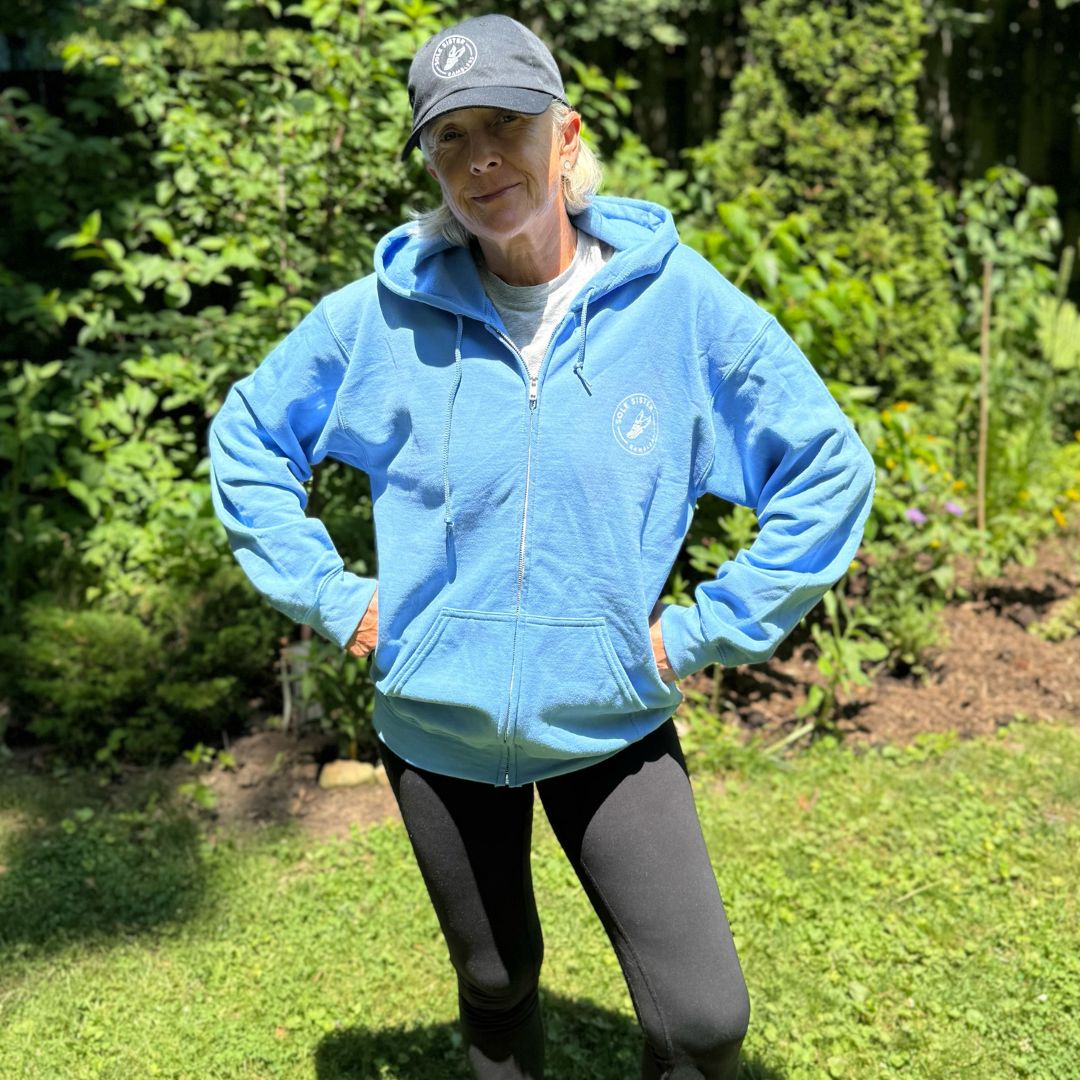 Front view of a women wearing  a light blue zip up hoodie with a white Sole Sister Rambler logo on the chest.