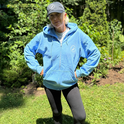 Front view of a women wearing  a light blue zip up hoodie with a white Sole Sister Rambler logo on the chest.
