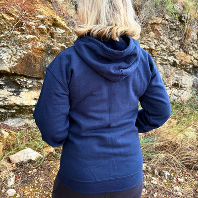 Back view of a navy blue zip up hoodie on woman standing outdoors.